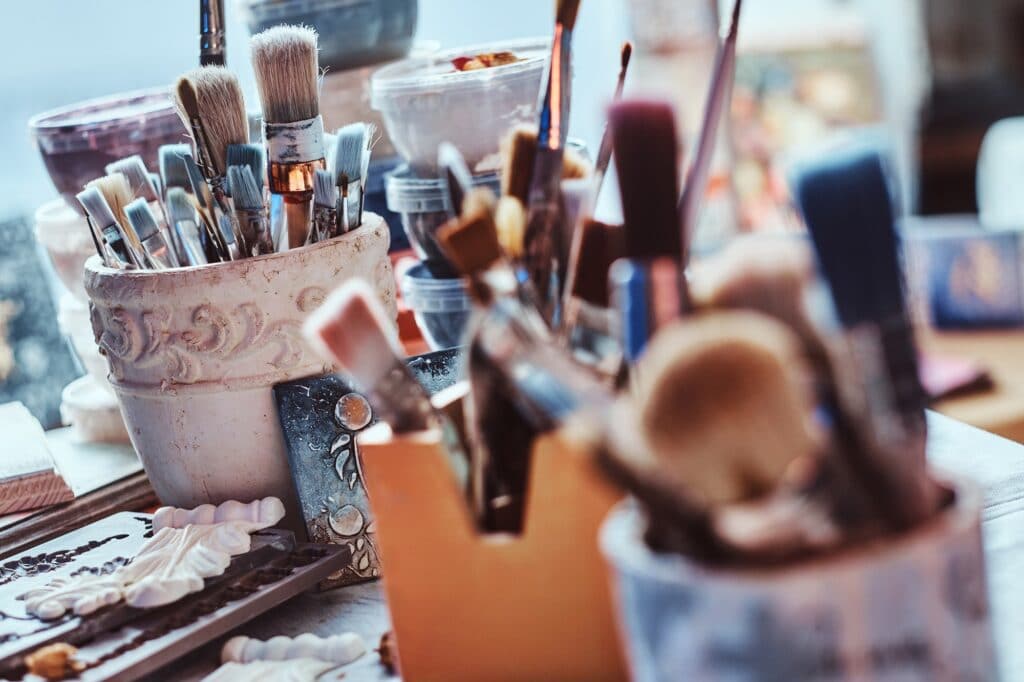 A lot of different brushes on artist's table in jars. There are artistick's mess on the table