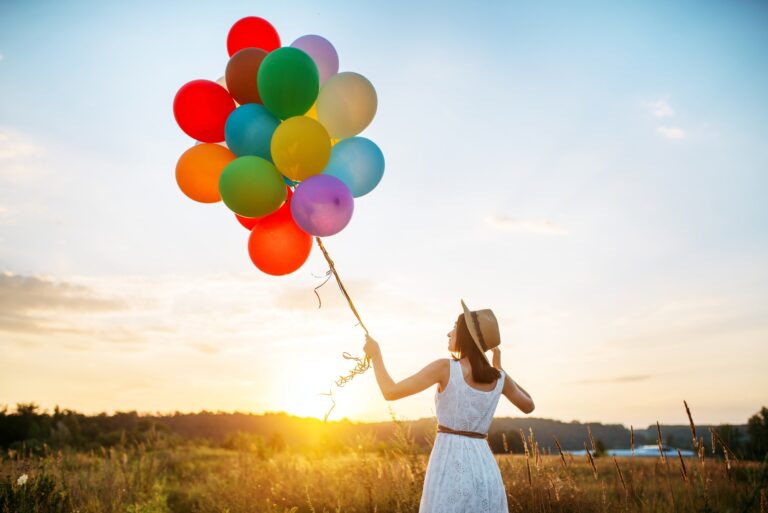 Girl with colorful balloons walking in wheat field